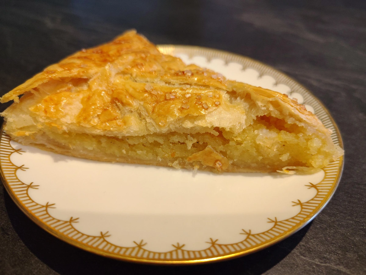 A cut piece on a small gold rimmed plate. It's a flat sort of cake with almond-sugar filling and flaky puff pastry lid.